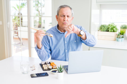 Handsome Business Senior Man Eating Delivery Sushi While Working Using Laptop With Angry Face, Negative Sign Showing Dislike With Thumbs Down, Rejection Concept