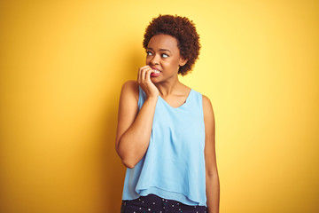 Beautiful african american woman wearing elegant shirt over isolated yellow background looking stressed and nervous with hands on mouth biting nails. Anxiety problem.