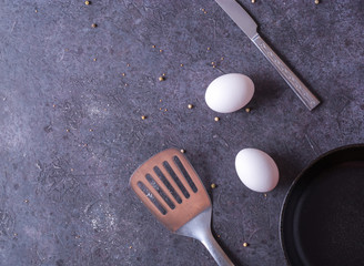 Frying pan and eggs. Empty cast iron pan, eggs, salt, pepper, oil and parsley on black background...