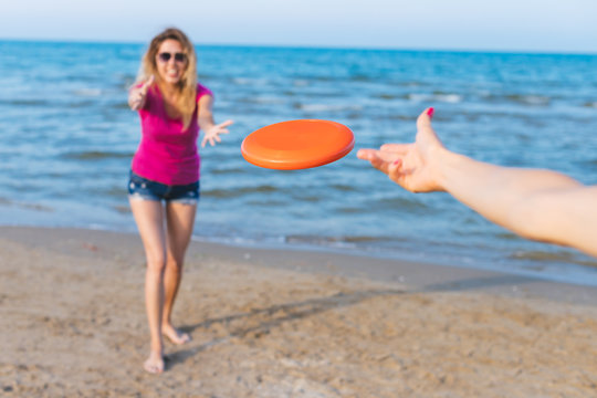 Millennials girls playing on the beach, focus on red frisbee