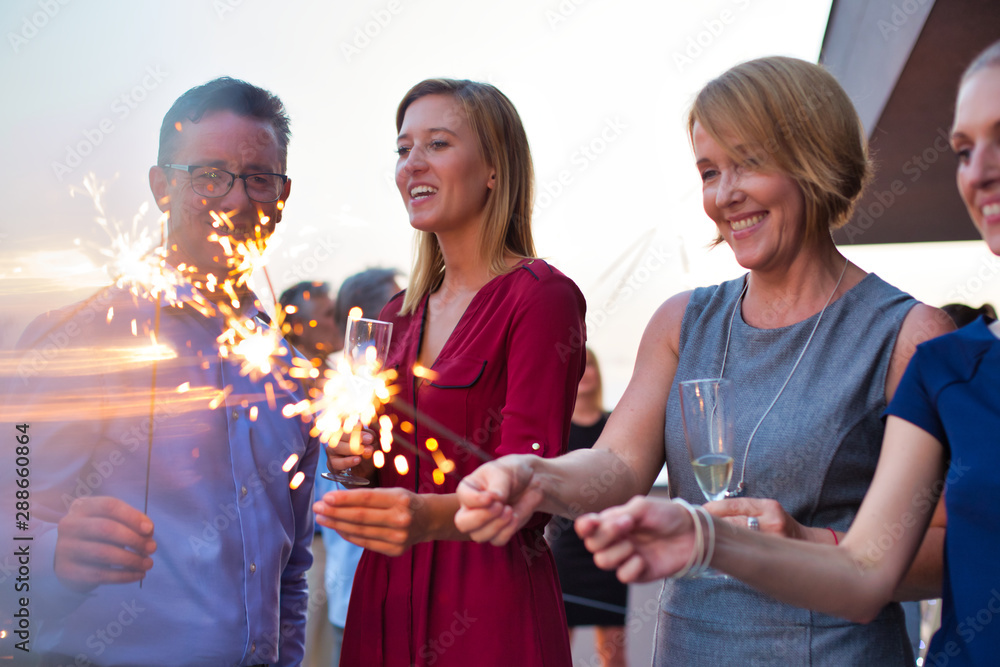 Wall mural smiling business colleagues holding sparklers during party on rooftop