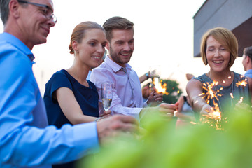 Smiling business colleagues holding sparklers during party on rooftop