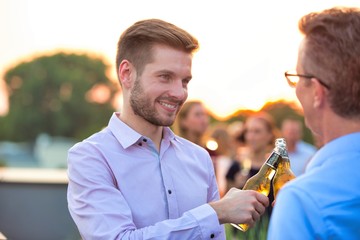Businessmen toasting beer bottles during success party on rooftop