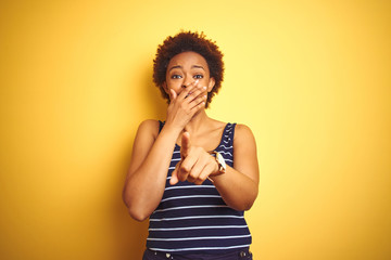 Beauitul african american woman wearing summer t-shirt over isolated yellow background laughing at you, pointing finger to the camera with hand over mouth, shame expression