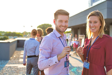 Portrait of smiling young business colleagues standing with wineglasses at rooftop party