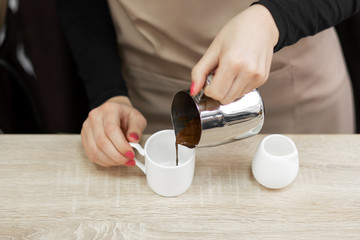 An apron barista pours hot cocoa into a cup. Barista work in a coffee shop