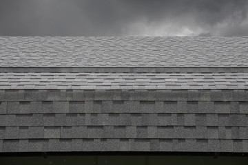 wet black shingle roof while raining dark. asphalt tiles on the roof on cloudy day.