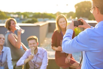 Businessman photographing colleagues during rooftop success party