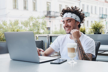 Excited hipster guy with dreadlocks hairstyle rejoice in winning an internet lottery made bets on website on laptop. Handsome bearded man celebrating victory in online competitions enjoying success