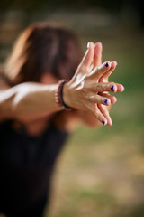 Focused Caucasain woman standing in Warrior III yoga pose. Nature exterior. Selective focus on hands.