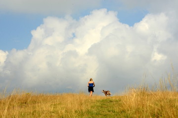 Dem Himmel so nah. Rückenansicht einer jungen frau mit Hund auf einer Wiese mit Wolken