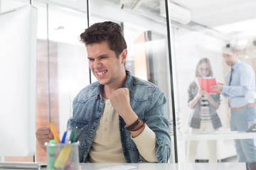 Excited businessman celebrating success at computer desk in office