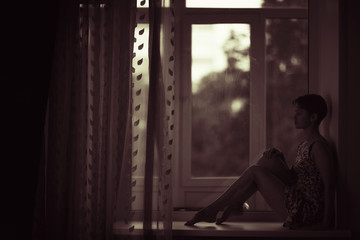 Silhouette of a dreamy girl sitting on a window