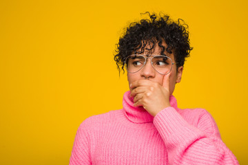 Fototapeta na wymiar Young african american woman wearing a pink sweater thoughtful looking to a copy space covering mouth with hand.