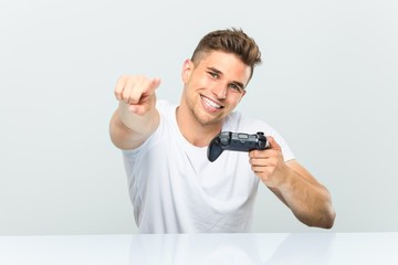Young man holding a game controller cheerful smiles pointing to front.