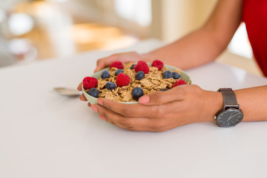 Close up of young woman eating healthy cereals and berries for breakfast