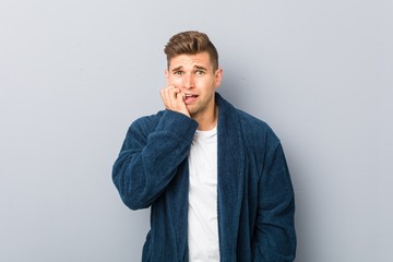 Young caucasian man wearing pajama biting fingernails, nervous and very anxious.