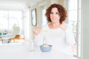 Obraz na płótnie Canvas Senior woman eating asian noodles using chopsticks pointing with finger to the camera and to you, hand sign, positive and confident gesture from the front