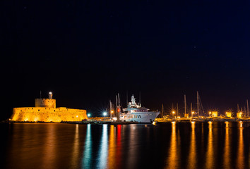 Night photo of ancient fortress and pier in Rhodes city on Rhodes island, Dodecanese, Greece. Stone walls and bright night lights. Famous tourist destination in South Europe