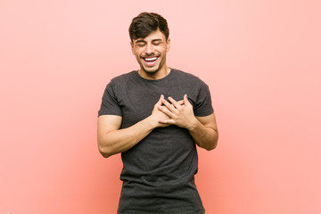 Young hispanic casual man laughing keeping hands on heart, concept of happiness.