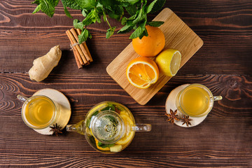 Hot tea with lemon, orange, ginger and mint on rustic wooden table in the morning