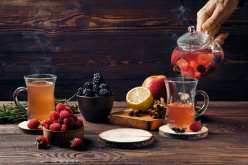 Pouring fruit tea with raspberries, bramble, apple and lemon in cup from teapot
