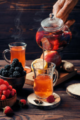 Pouring freshly brewed fruit and herbal tea from kettle into cup, dark mood.