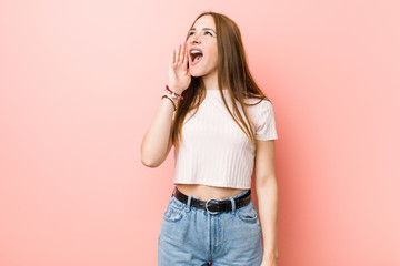 Young redhead ginger woman against a pink wall shouting and holding palm near opened mouth.