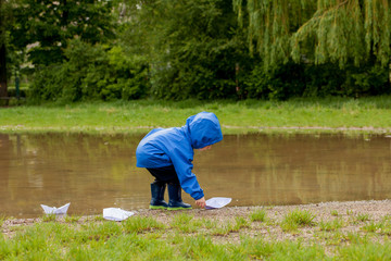 Portrait of cute kid boy playing with handmade ship. kindergarten boy sailing a toy boat by the waters' edge in the park
