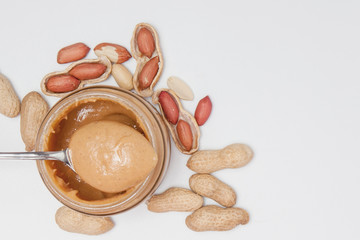 Creamy peanut butter in glass jar, peanut and spoon isolated on white background. A traditional product of American cuisine