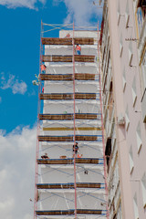 Scaffolding on a multistory building. Warming of the outer wall panel. A working man isolates the walls of a multistory building
