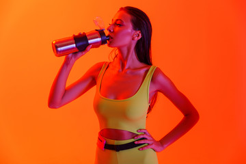 Photo of young brunette woman wearing formfitting sportswear drinking water from metal bottle while...