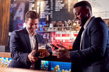 Two Businessmen Checking Mobile Phones Whilst Meeting For Drink In Bar