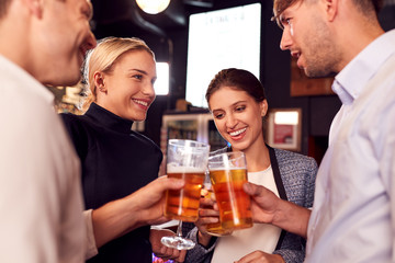 Male And Female Friends Making A Toast As They Meet For Drinks And Socializing In Bar After Work