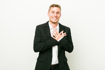 Young caucasian business man laughing keeping hands on heart, concept of happiness.