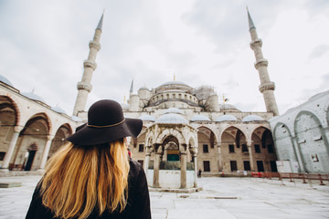 Young woman traveler in hat and black coat looking at the blue mosque in Istanbul, Turkey. A girl...