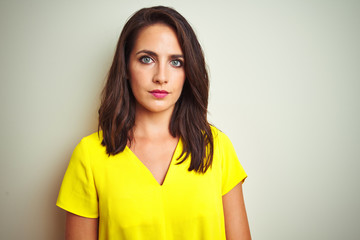 Young beautiful woman wearing yellow t-shirt standing over white isolated background with serious expression on face. Simple and natural looking at the camera.