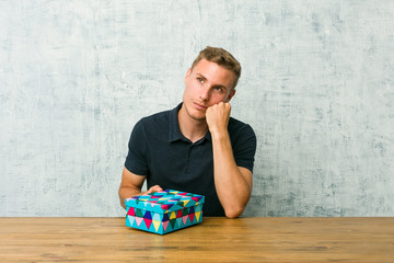 Fototapeta premium Young caucasian man holding a gift box on a table who feels sad and pensive, looking at copy space.
