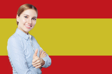 Happy student girl with thumb up against the spanish flag backgr