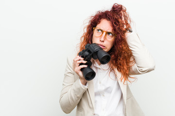 Young caucasian business redhead woman holding a binoculars being shocked, she has remembered...
