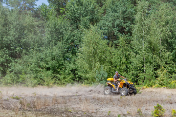 Man riding a yellow quad ATV all terrain vehicle on a sandy forest. Extreme sport motion, adventure, tourist attraction.