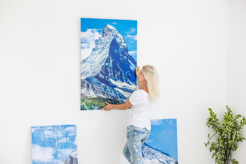Happy blonde woman hanging large picture on wall at home