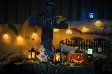 Halloween decorations concept at night. Close up of jack o'lantern, vintage lanterns, pumpkins, skull, autumn leaves. Colorful halloween lights on evening. Happy Halloween scene on wooden background