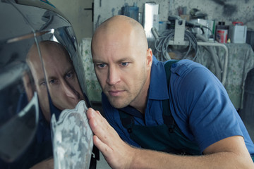 Man fixes car fender after crash and prepares the paint for the car in a car service. Repairman fix...