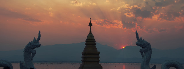 Sunset behind mountains at lake with buddhist temple and dragons in thailand.