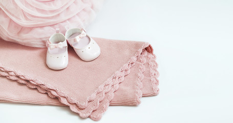 Pink baby plaid decorated with lace. Pink pillow lies nearby. White baby shoes stand on a plaid.