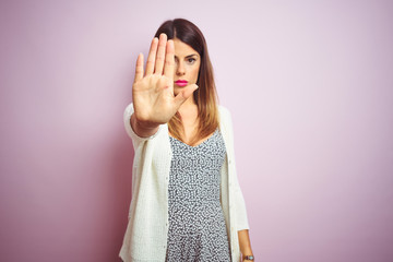 Young beautiful woman standing over pink isolated background doing stop sing with palm of the hand....