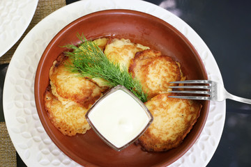 Potato pancakes in a clay plate with sour cream and dill