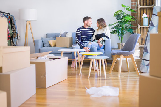Young beautiful couple sitting on the sofa drinking cup of coffee at new home around cardboard boxes