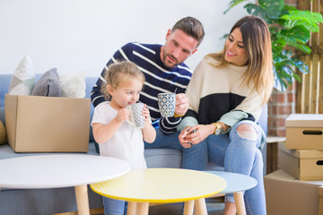 Obraz na płótnie Canvas Beautiful family, parents sitting on the sofa drinking coffee looking his kid playing at new home around cardboard boxes